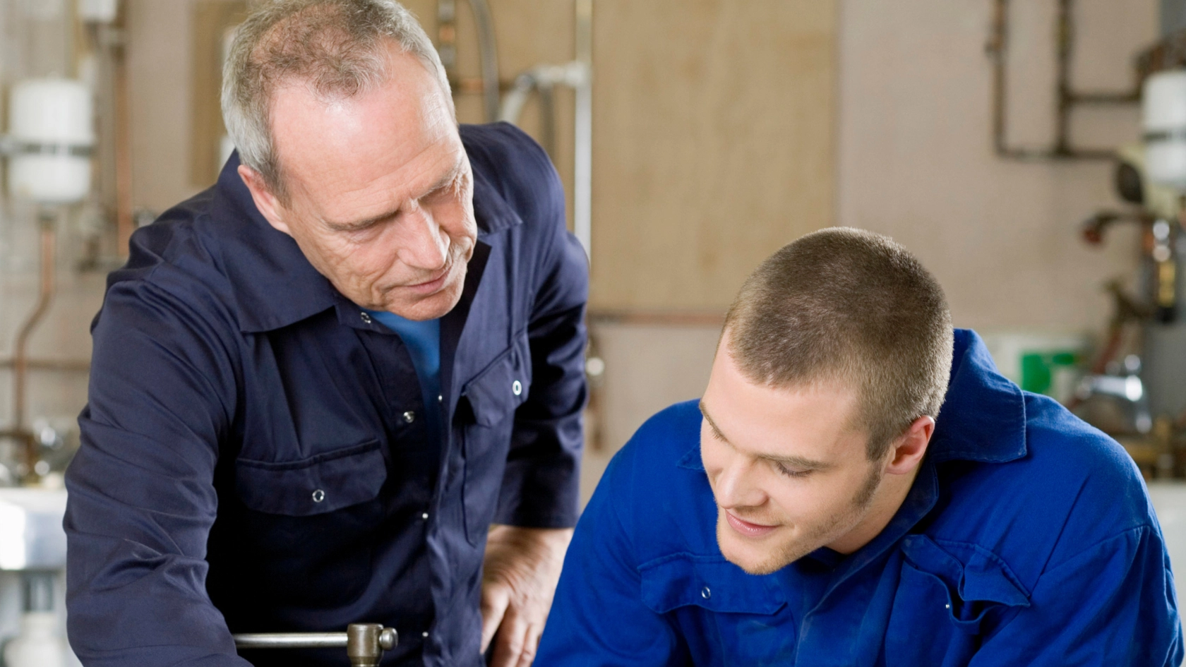 Ein Auszubildender zum Gas-Wasser Installateur bekommt von seinem Meister etwas erklärt.