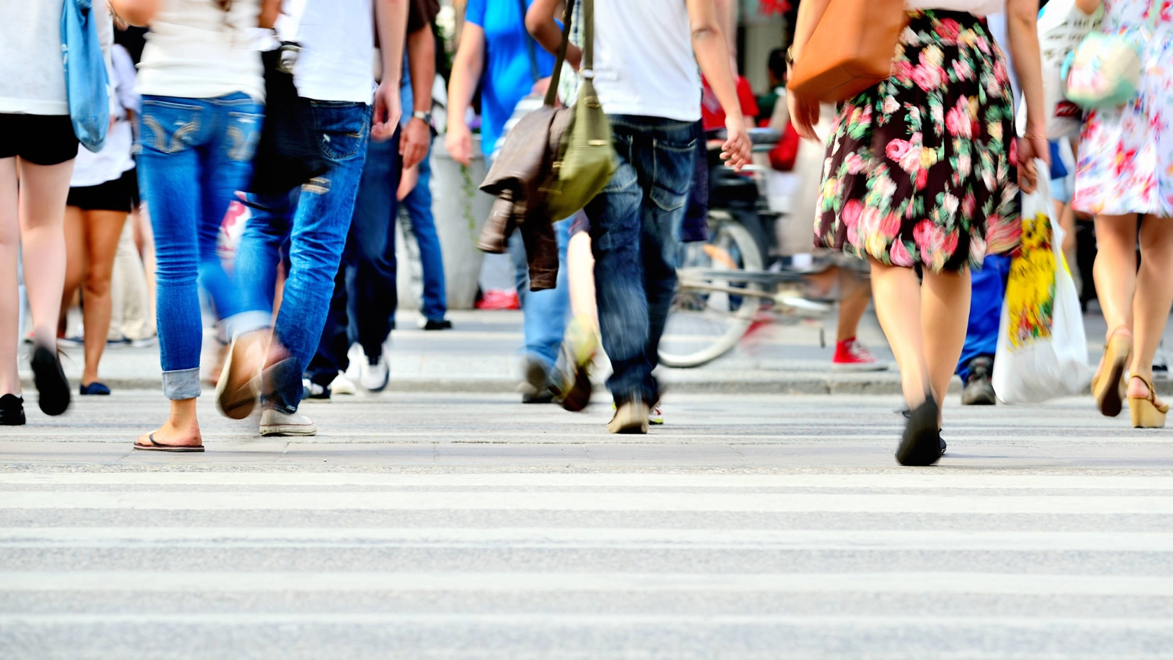 Beine von Fußgängern, die über einen Zebrastreifen gehen.